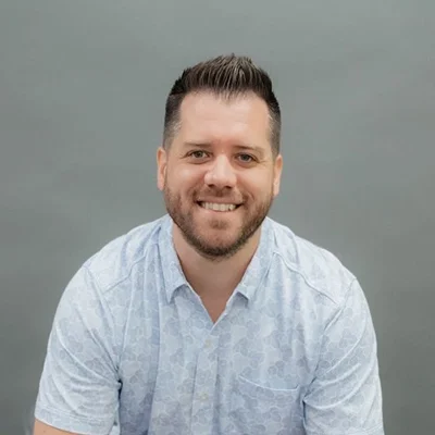 Chiropractor Andy Joyce Smiling In Front Of Grey Backdrop
